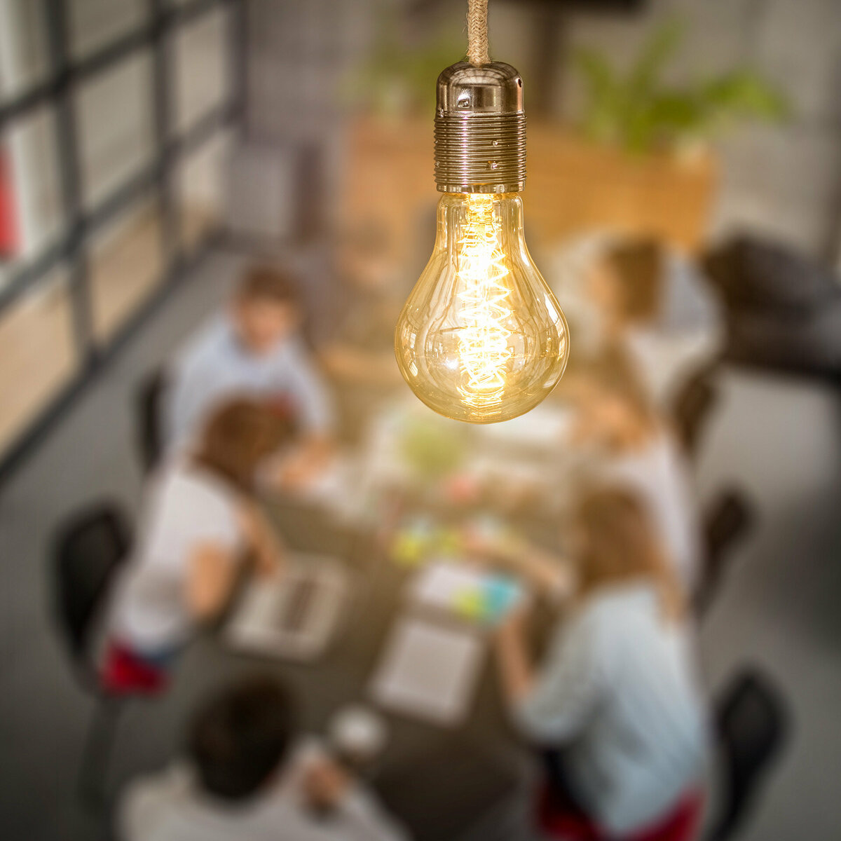 A bright light bulb. Faintly in the background a group of business people work together at a large table