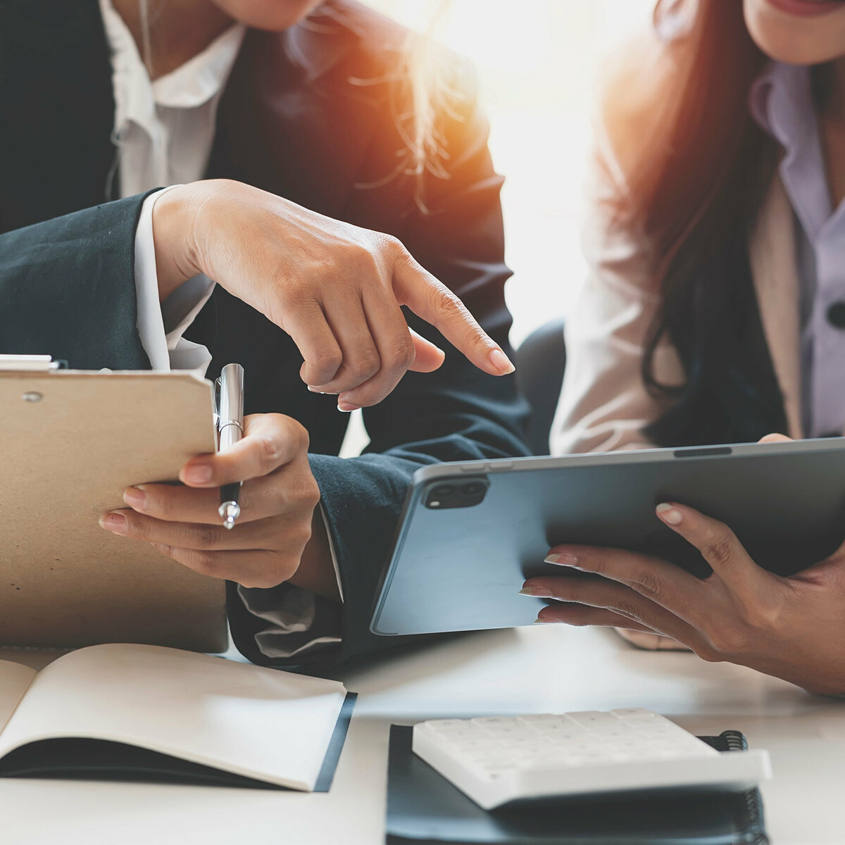 Coworkers working together in boardroom holding a tablet and clipboard