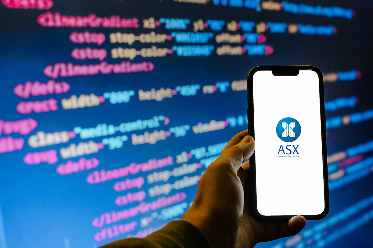 ASX Australian Securities Exchange. Hand holding phone in front of screen with code