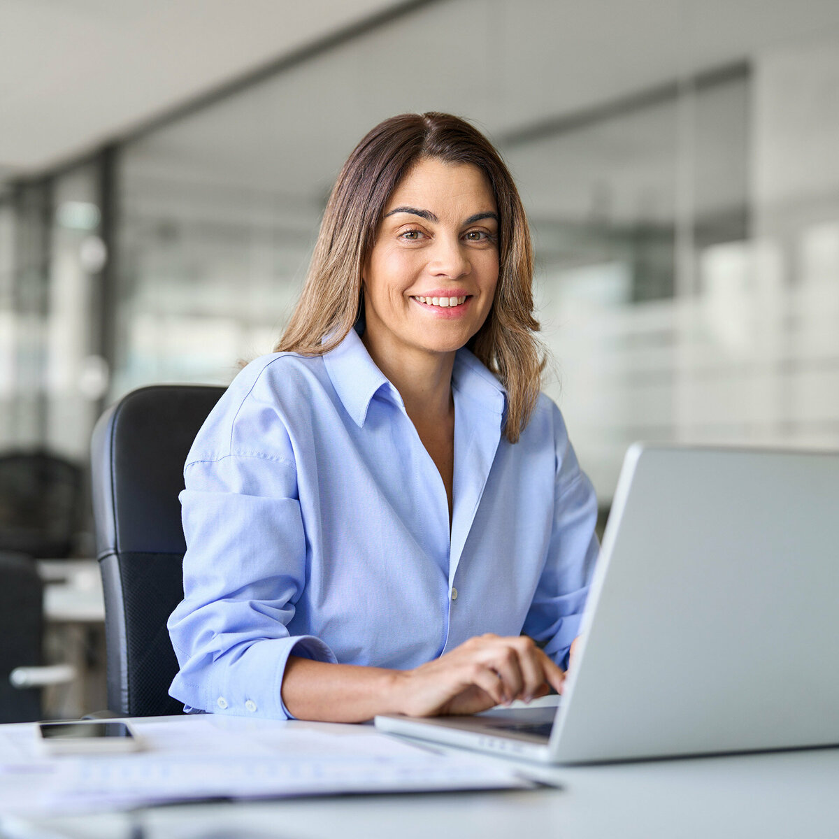 A business woman sitting at a desk with her laptop open. She is smiling.