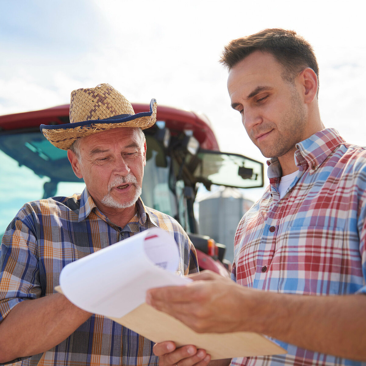 Two farmers assessing data on a clipboard in front of a tractor.